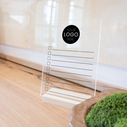A minimalist to do list printed on clear acrylic with a wooden stand.